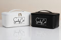 Two different color  rectangular cosmetic cases on a reflective white surface against a warm beige background. The left case is white with black trim and a white handle, and the right case is black with a black handle.
